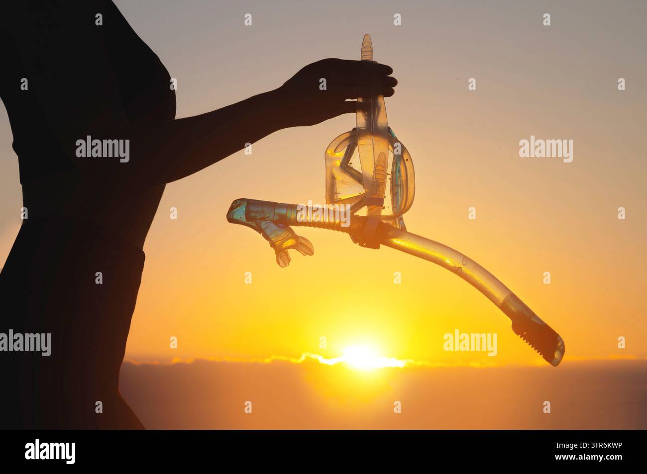 Strandabenteuer, Handsilhouette mit Schnorgerausrüstung. Unerkennbare Frau hält eine Unterwassermaske und einen Schnorchel in der Hand bei Sonnenuntergang Stockfoto