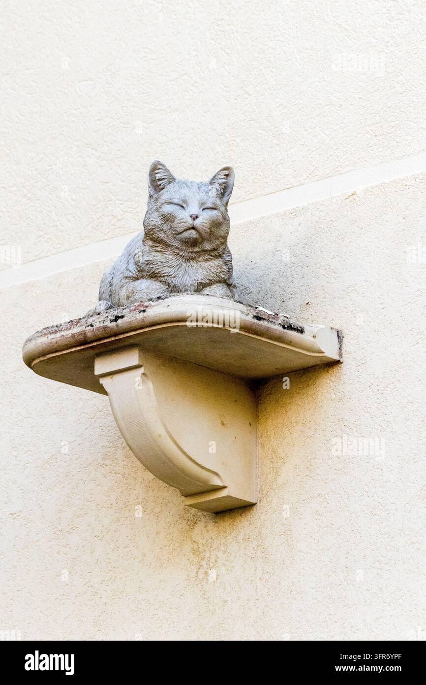 Steinerne Katzenstatue auf dekorativem Wandregal vor texturierter beiger Stuckwand Stockfoto