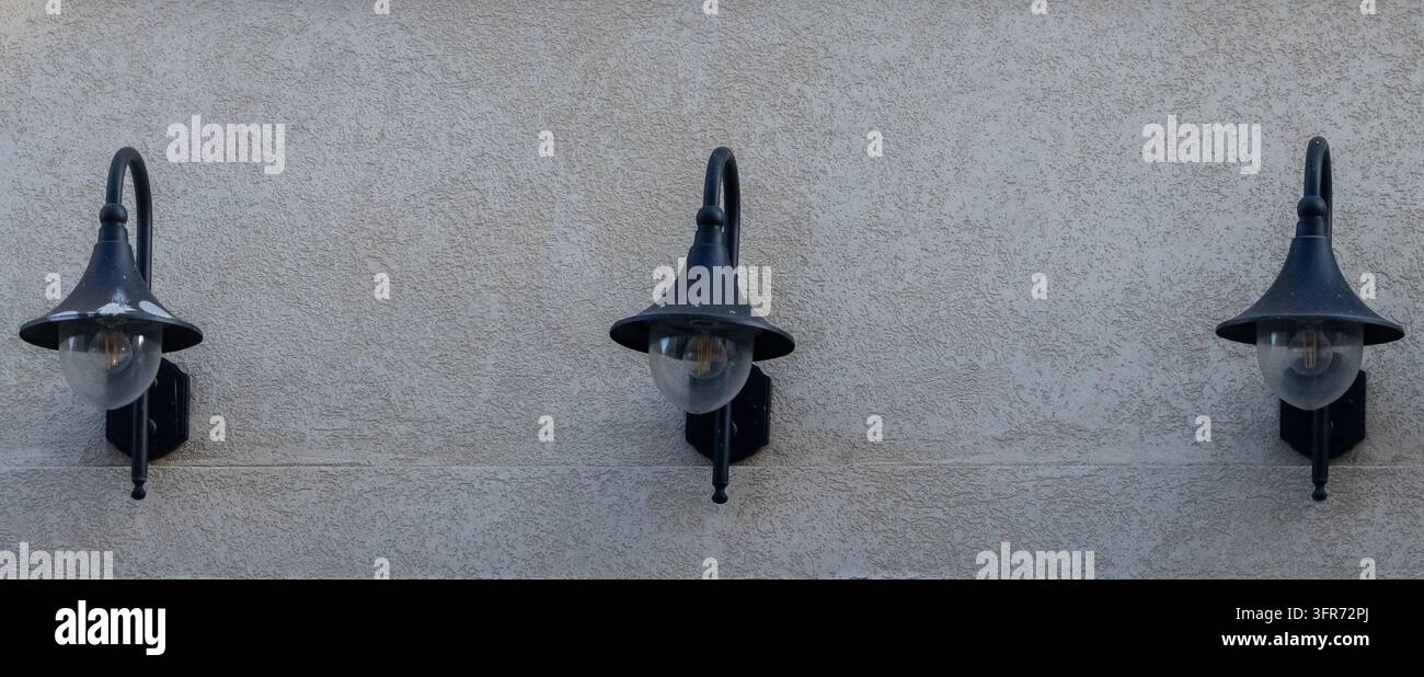 Drei antike Außenwandleuchten montiert an einer Putz-Außenwand mit symmetrischem Abstand Stockfoto