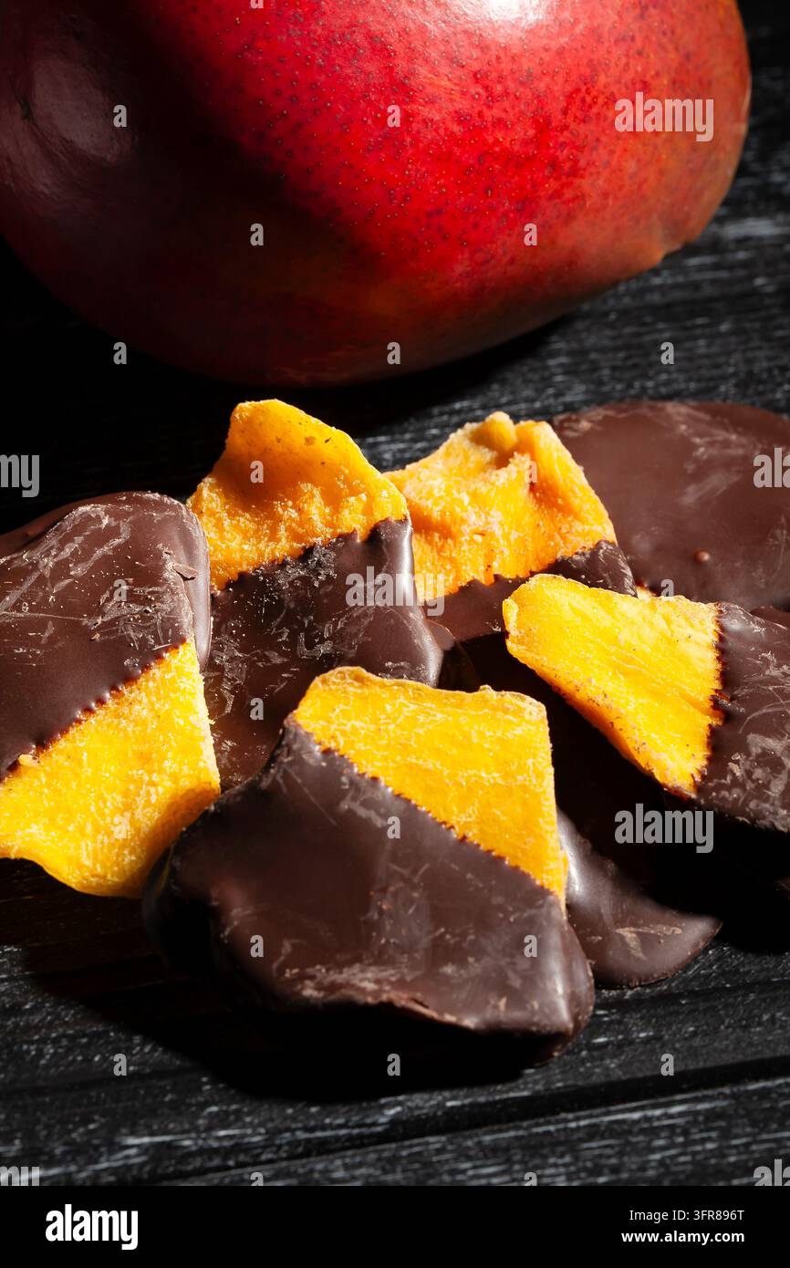 Schokoladengetaufter Mango auf schwarzem Holzgrund Stockfoto