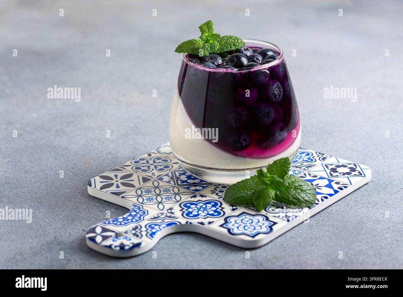 Hausgemachtes geschichtetes Beerendessert - Panna Cotta mit Beeren- und Sahnegelee, Blaubeeren in einem Glas auf einer Porzellanservierplatte Stockfoto