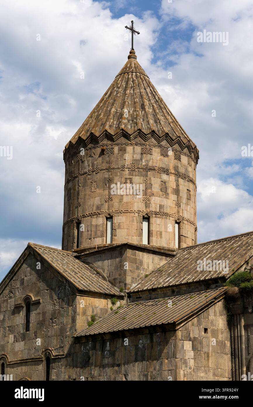 Nahaufnahme des steinernen Glockenturms und des eisernen Kreuzes des Tatev-Klosters vor den bewaldeten Bergen, Syunik-Provinz, Tatev, Armenien Stockfoto