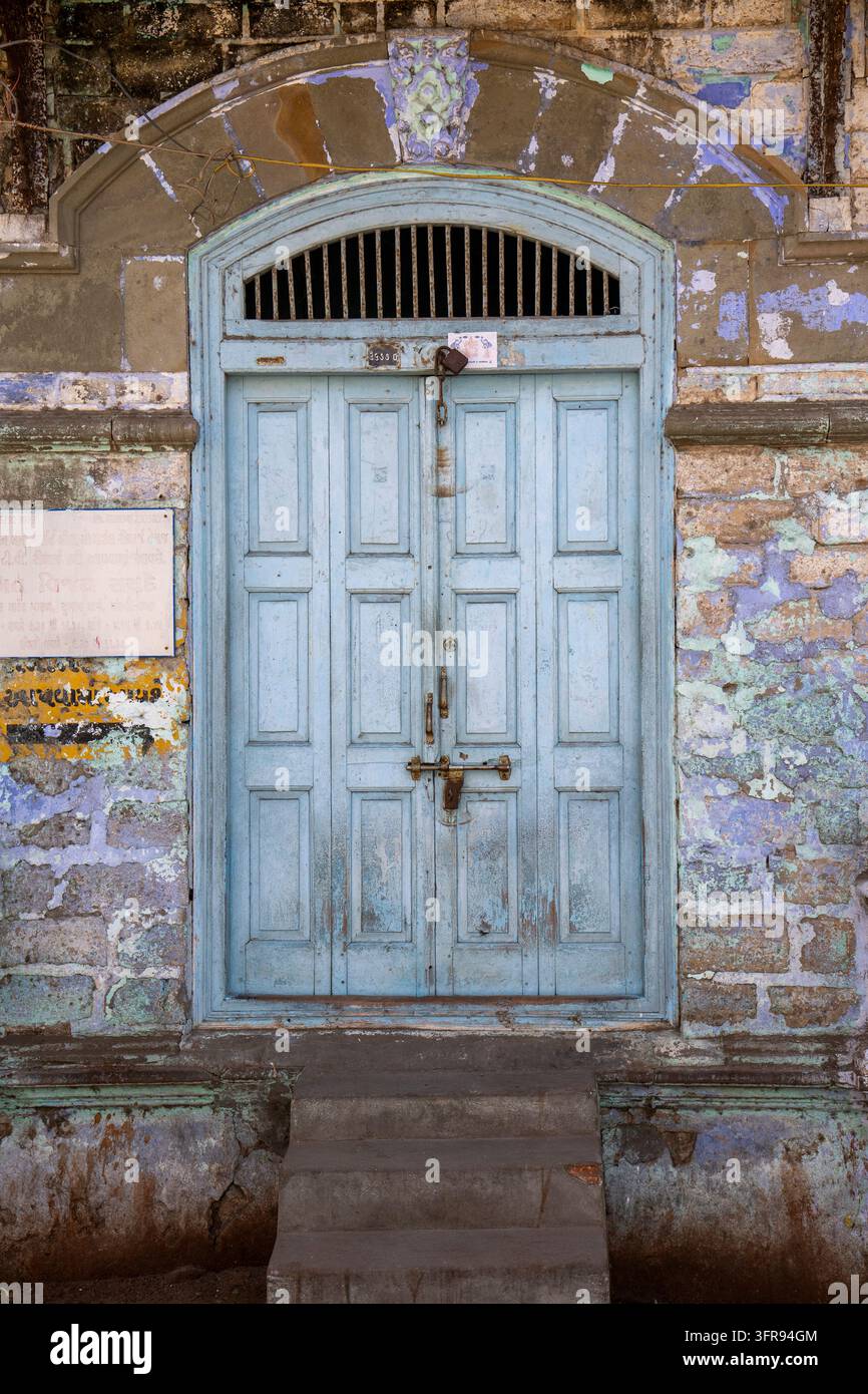Eine hellblaue Holzpaneeltür befindet sich in einem gewölbten Steinrahmen oben auf abgenutzten Stufen, Gujarat, Mandvi, Indien Stockfoto