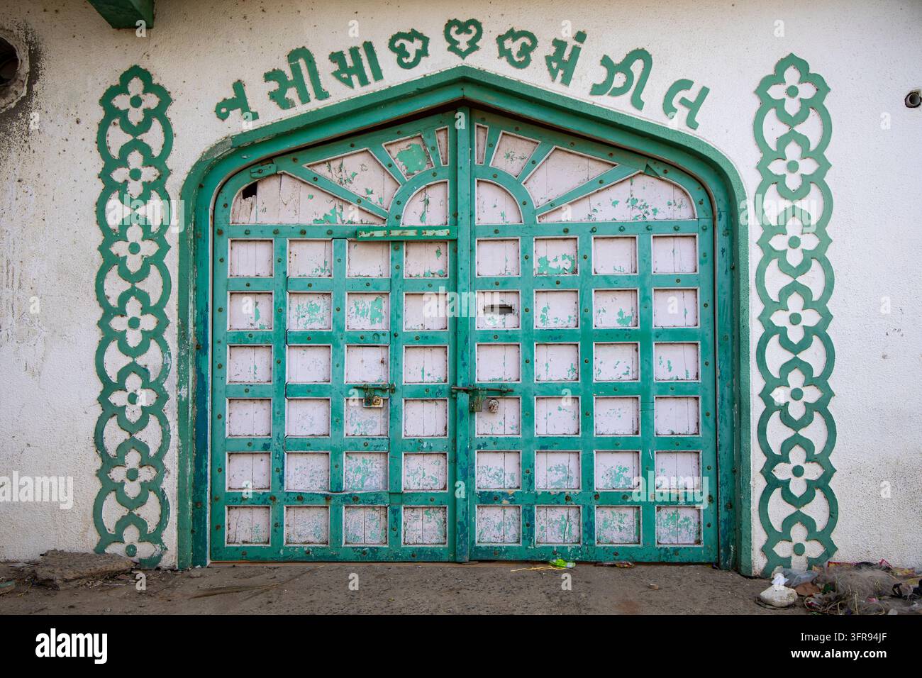 Verschnörkelte grüne Holztür mit geschnitzten Blumenpaneelen und gujaratischer Inschrift oben, Gujarat, Mandvi, Indien Stockfoto