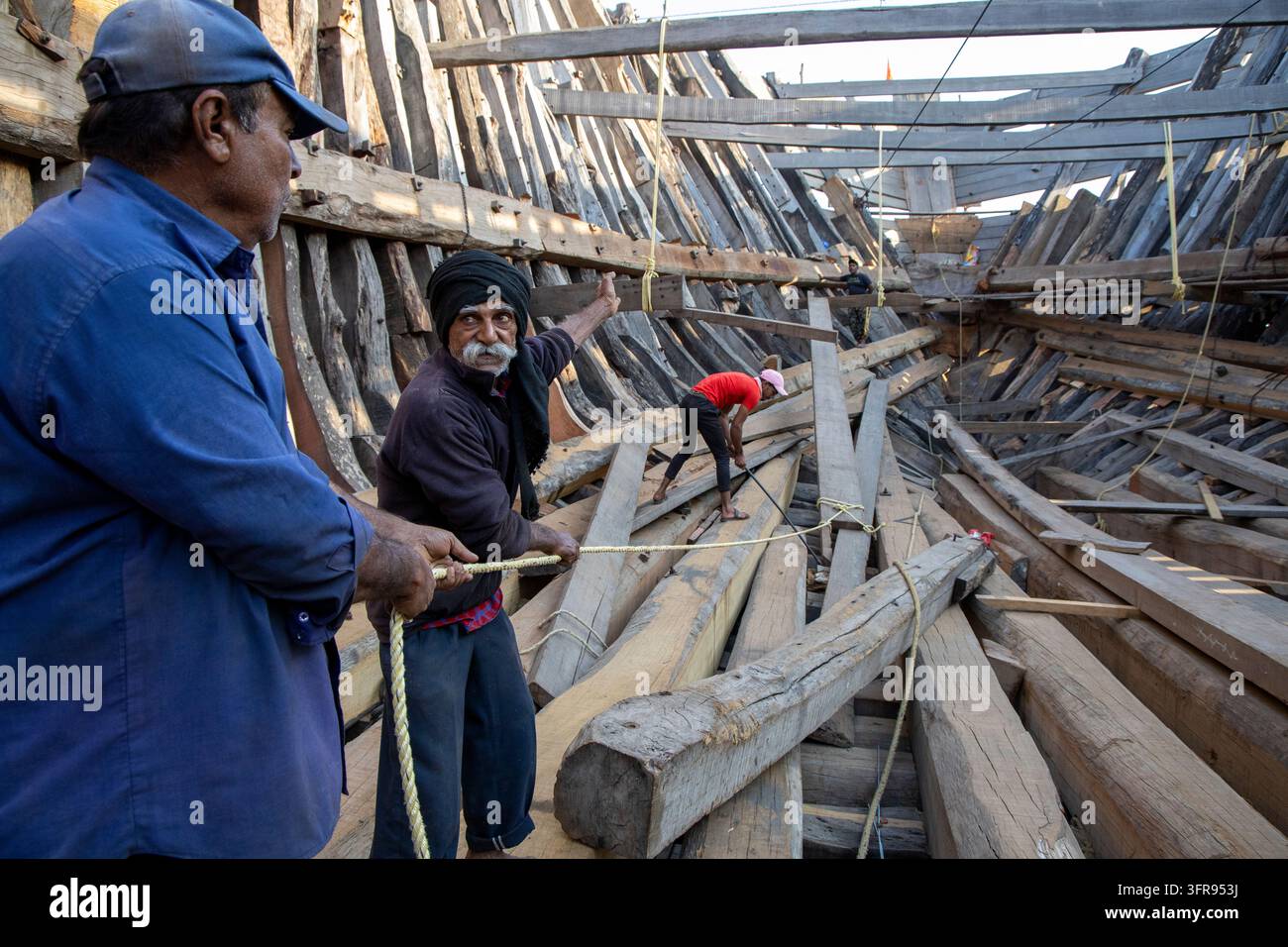 Drei Schiffbauer reparieren den Holzrahmen eines traditionellen Dhow in einer Küstenwerft, Gujarat, Mandvi, Indien Stockfoto