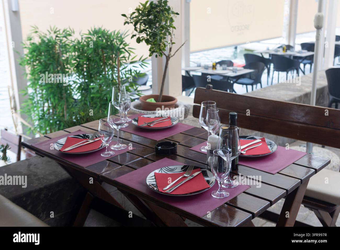 30. Juni 2026, Budva, Montenegro, Ein elegant gedeckter Restauranttisch zeigt rote Servietten, Glasgeschirr und Besteck, das ordentlich angeordnet ist. Der Holztisch ist Stockfoto