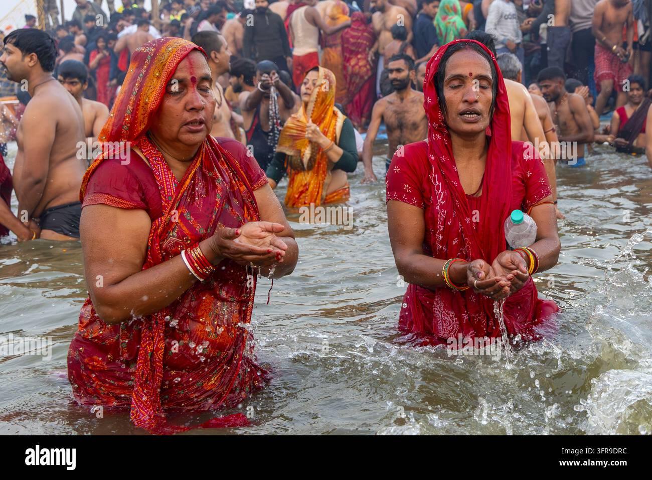 Zwei Frauen in roten Saris mit geschlossenen Augen halten Flusswasser in hohlen Händen im Gebet am Sangam, Uttar Pradesh, Prayagraj, Indien Stockfoto
