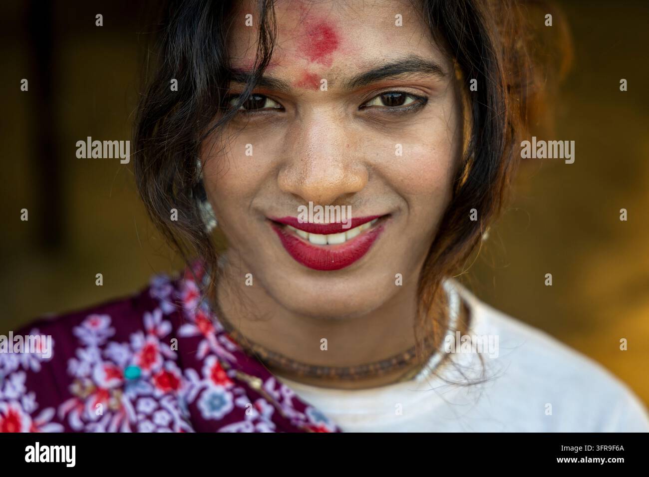 Lächelnde Hijra mit rotem Lippenstift und rotem Bindi, trägt einen Blumenschal und ein weißes Oberteil bei der Maha Kumbh Mela, Uttar Pradesh, Prayagraj, Indien Stockfoto