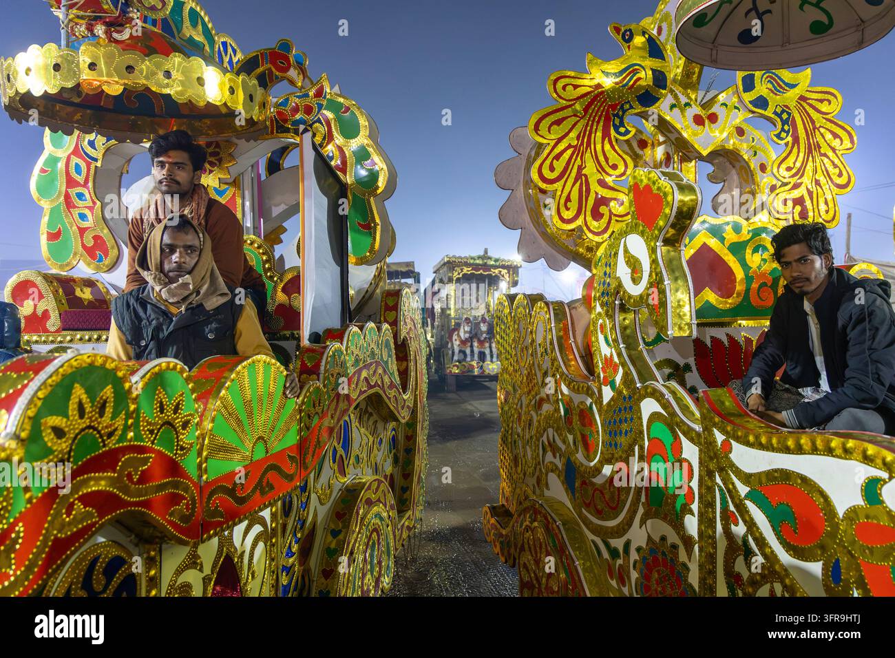 Drei Männer sitzen auf zwei kunstvoll goldverzierten Wagen mit farbenfrohen Mustern auf einer Straße in der Dämmerung, Uttar Pradesh, Prayagraj, Indien Stockfoto