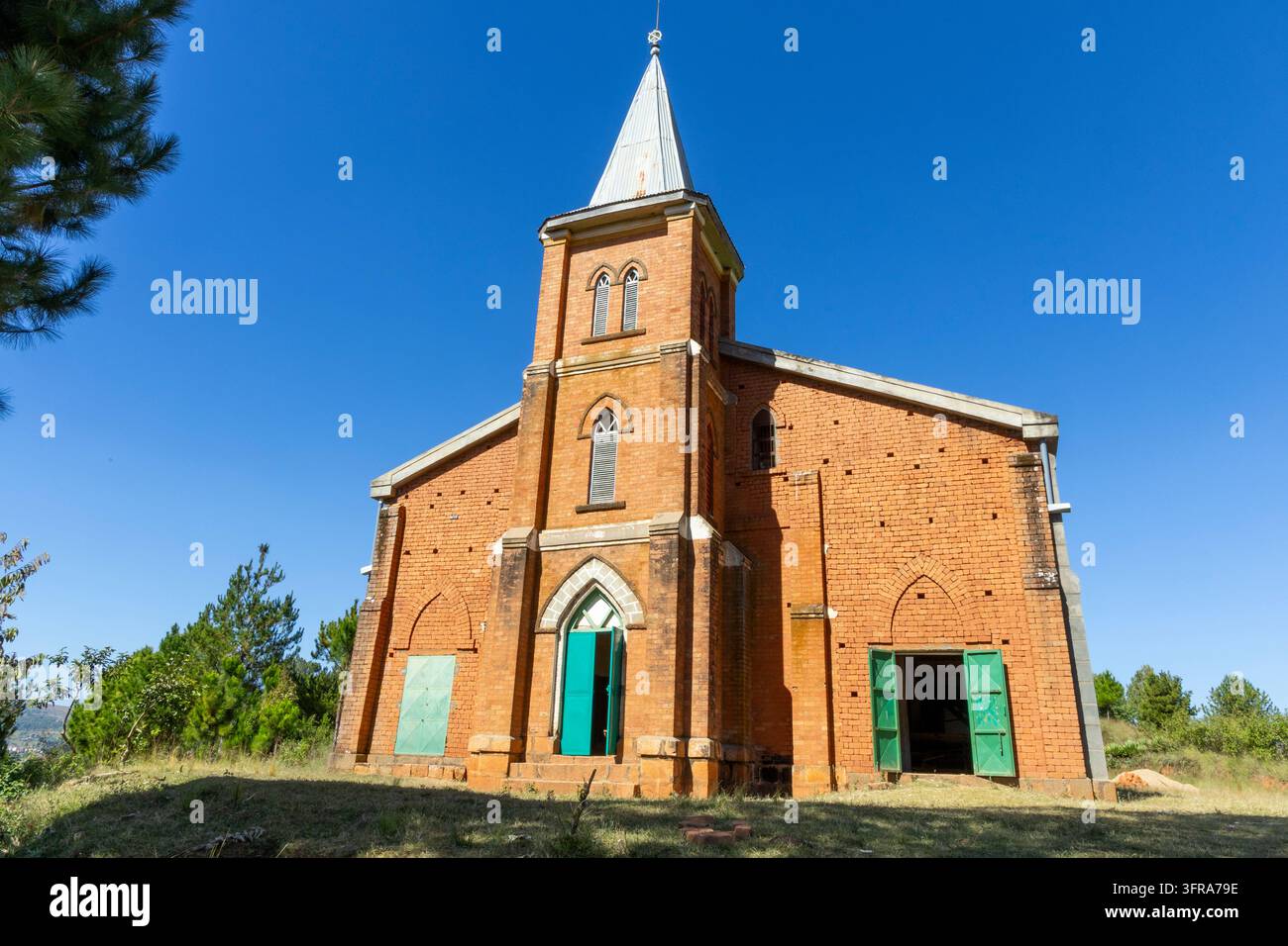 Eine rote Backsteinkirche mit einem hohen Turm und grünen Türen steht unter einem klaren blauen Himmel, Vakinankaratra, Antsirabe, Madagaskar Stockfoto