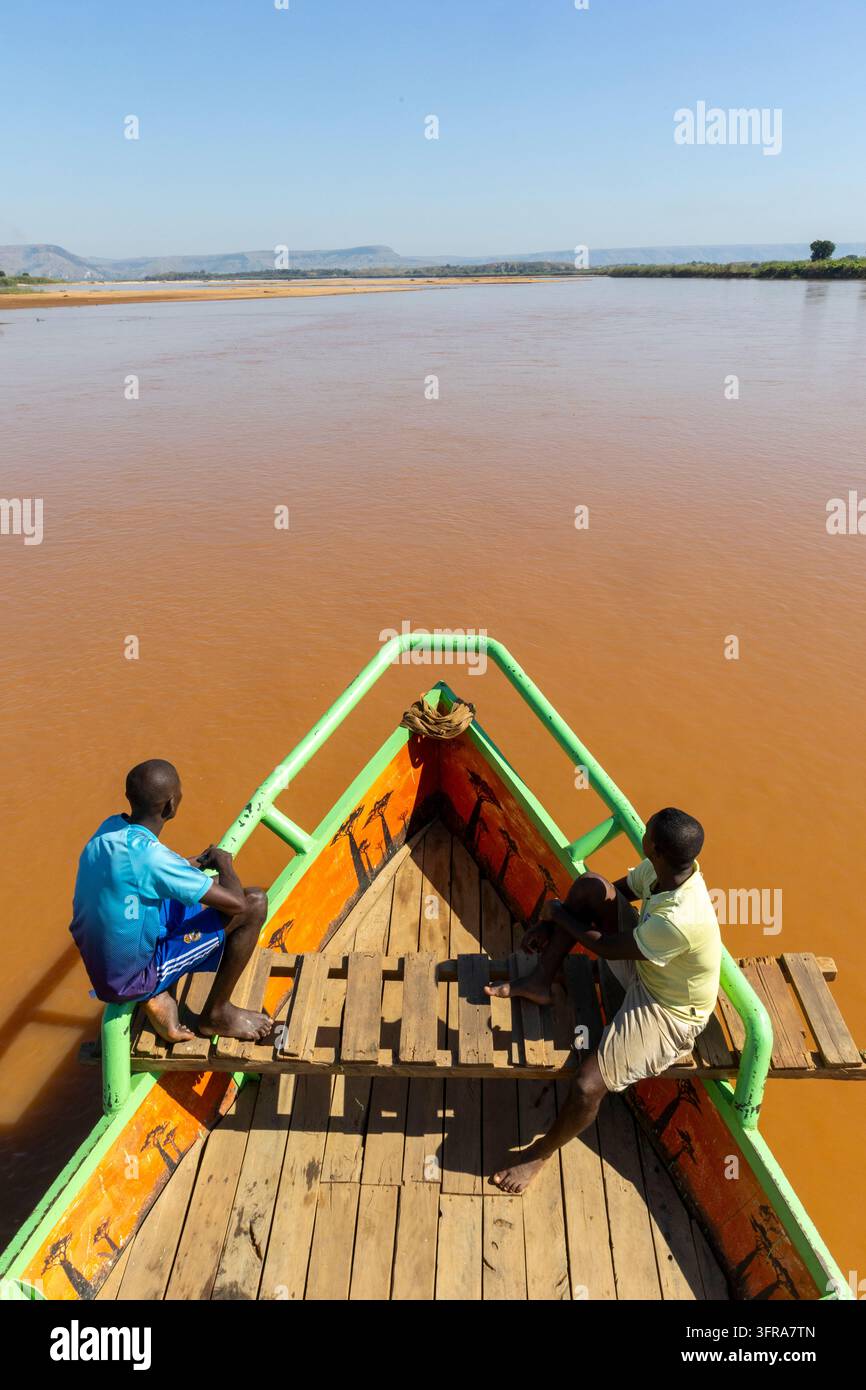 Zwei junge Männer sitzen auf dem bemalten Bug eines Flusskreuzfahrtschiffes mit Blick auf ein weites Tal, Menabe, Tsiribihina, Madagaskar Stockfoto