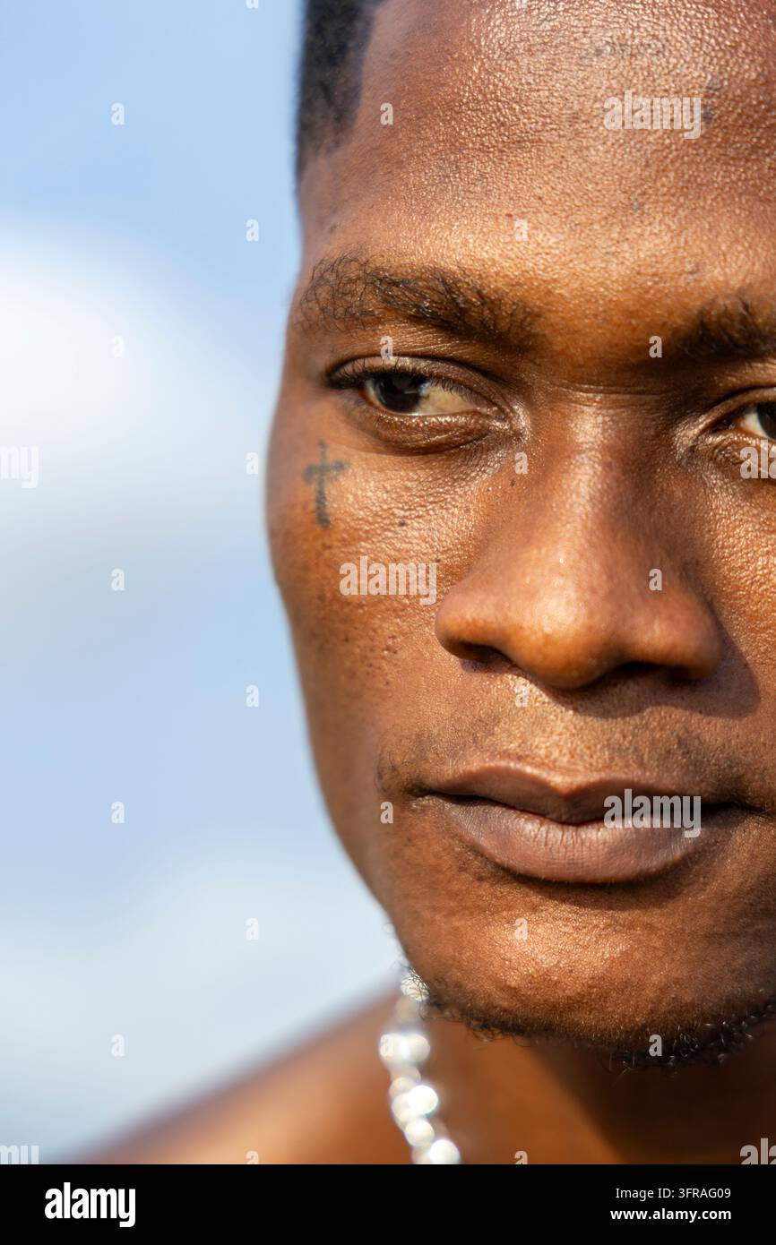 Nahaufnahme eines Mannes mit einem kleinen Kreuz-Tattoo unter dem Auge am Strand, Maritime Region, Lome, Togo Stockfoto