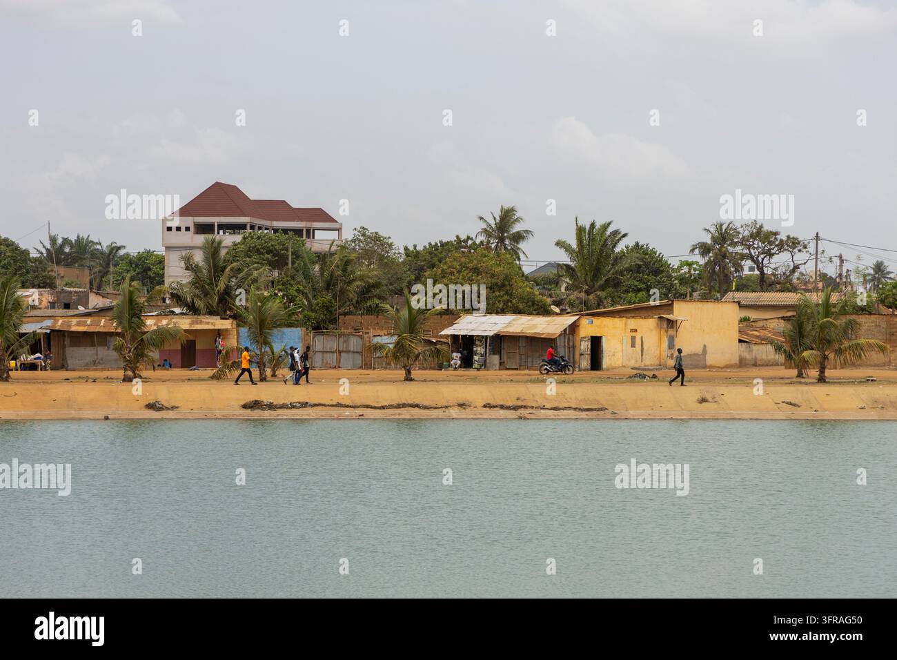 Menschen schlendern entlang einer Seeuferpromenade, die von Häusern und Palmen gesäumt ist, Maritime Region, Lomé, Togo Stockfoto