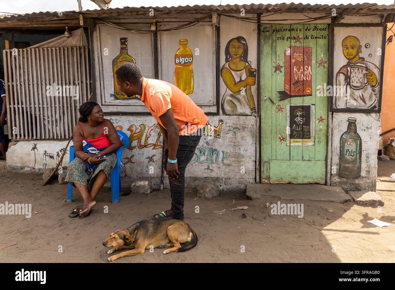 Mann spricht mit einer sitzenden Frau vor einer Ladenwand, die mit Getränken bemalt ist, Maritime Region, Lome, Togo Stockfoto