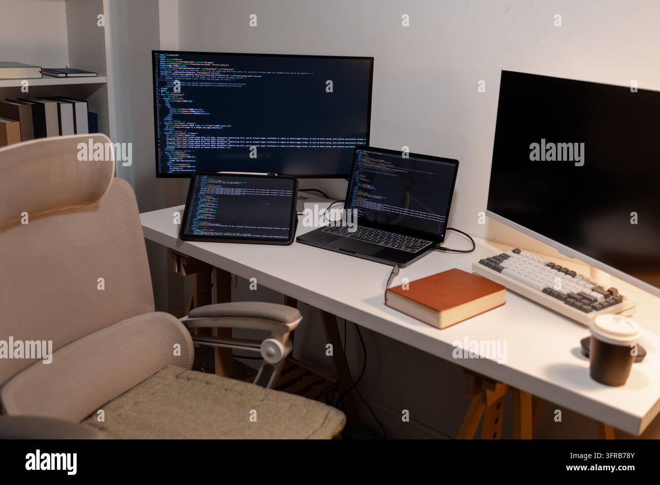 Moderner Arbeitsplatz für Softwareentwickler mit Laptop, Tablet, Dual-Monitoren, die Programmiercode anzeigen, und Bürotisch. Technologie, Codierung, Remote-Arbeit, Stockfoto