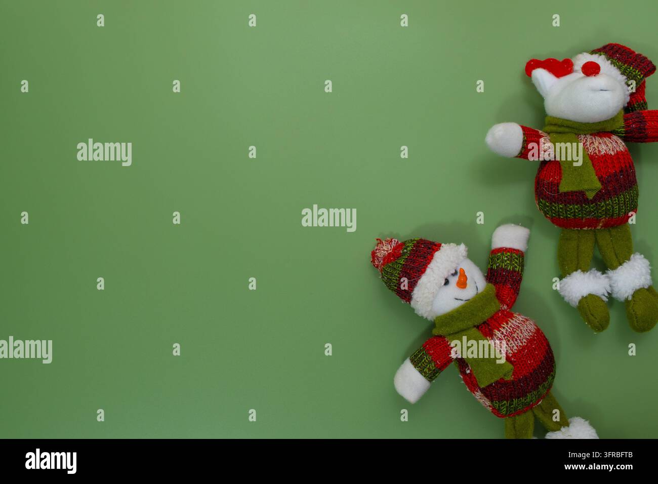 Zwei festliche Schneemann-Ornamente mit gestrickten Mützen und Schals auf grünem Hintergrund Stockfoto