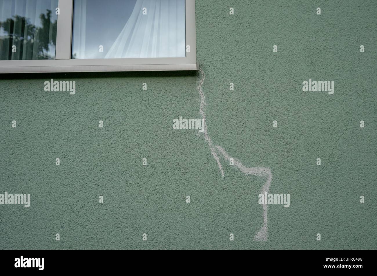 Ein gesprungenes Fenster in der Außenwand eines Gebäudes, das Sachschäden und mögliche Versicherungsansprüche veranschaulicht. Das beschädigte Glas hebt Risiken hervor, a Stockfoto