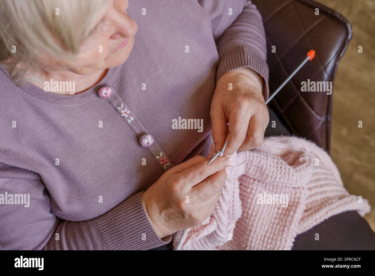 Eine ältere Frau sitzt auf einem Stuhl und strickt einen Wollartikel. Das Konzept eines Hobbys für aktives Altern, Langlebigkeit und geistige Gesundheit Stockfoto