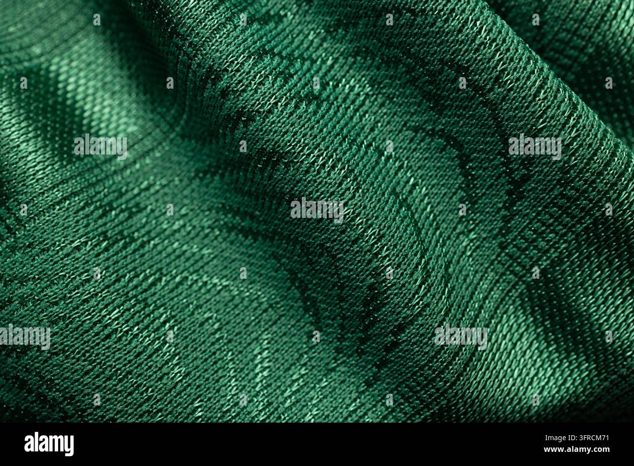 Dunkle smaragdgrüne Stofftextur mit fließenden Falten und gewebtem Muster in der Nahaufnahme Stockfoto