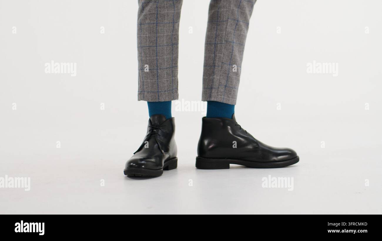 Mann trägt stilvolle Chukka-Stiefel, blaue Socken und graue karierte Hosen für moderne Herrenmode und Business-Kleidung Stockfoto