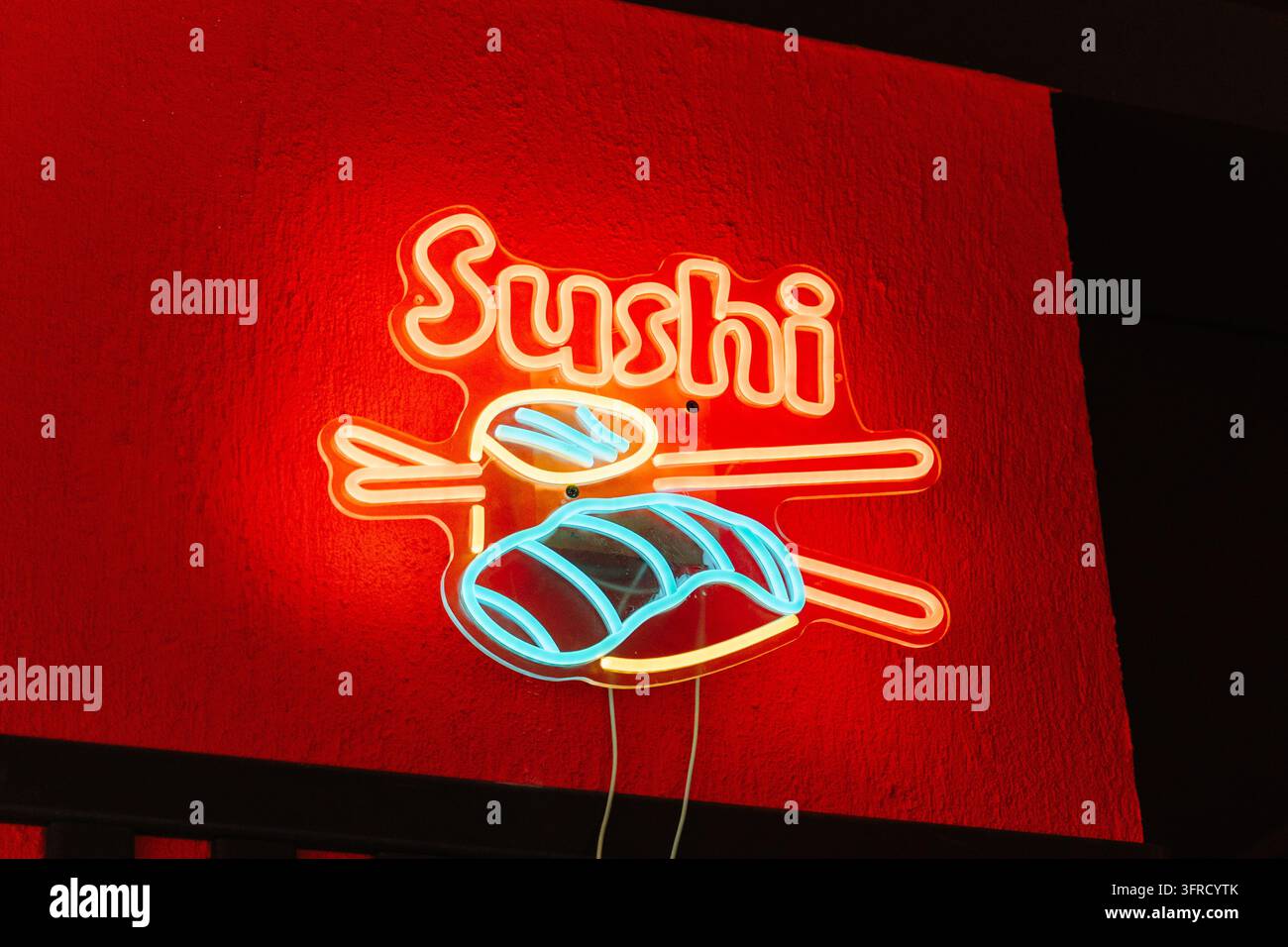 Ein farbenfrohes Neon-Sushi-Schild leuchtet vor einer strukturierten roten Restaurantwand. Repräsentiert japanische Küche, Restaurantmarken, Gastgewerbe und modernes Dinieren Stockfoto