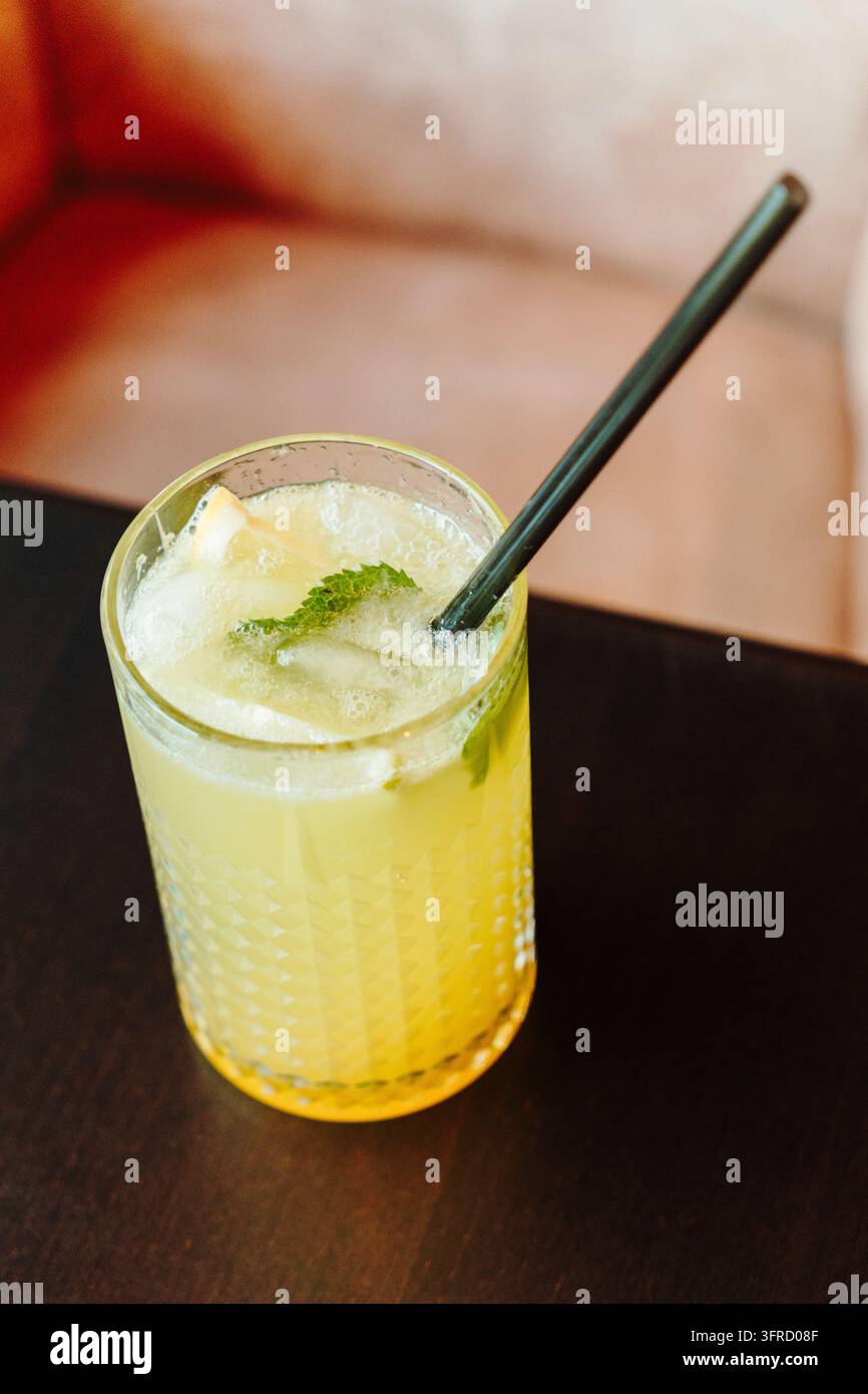 Eine Nahaufnahme aus der Vogelperspektive zeigt einen gelben Zitruscocktail mit Eis, Zitrone und Minze in einem gemusterten Glas. Stellvertretend für erfrischende Sommergetränke, Mixologie a Stockfoto
