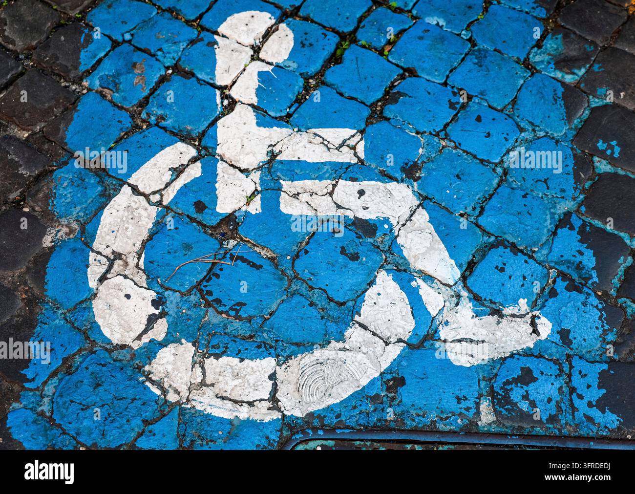 Rollstuhlsymbol markiert einen barrierefreien Parkplatz auf einer abgenutzten blau-weißen gepflasterten Oberfläche Stockfoto
