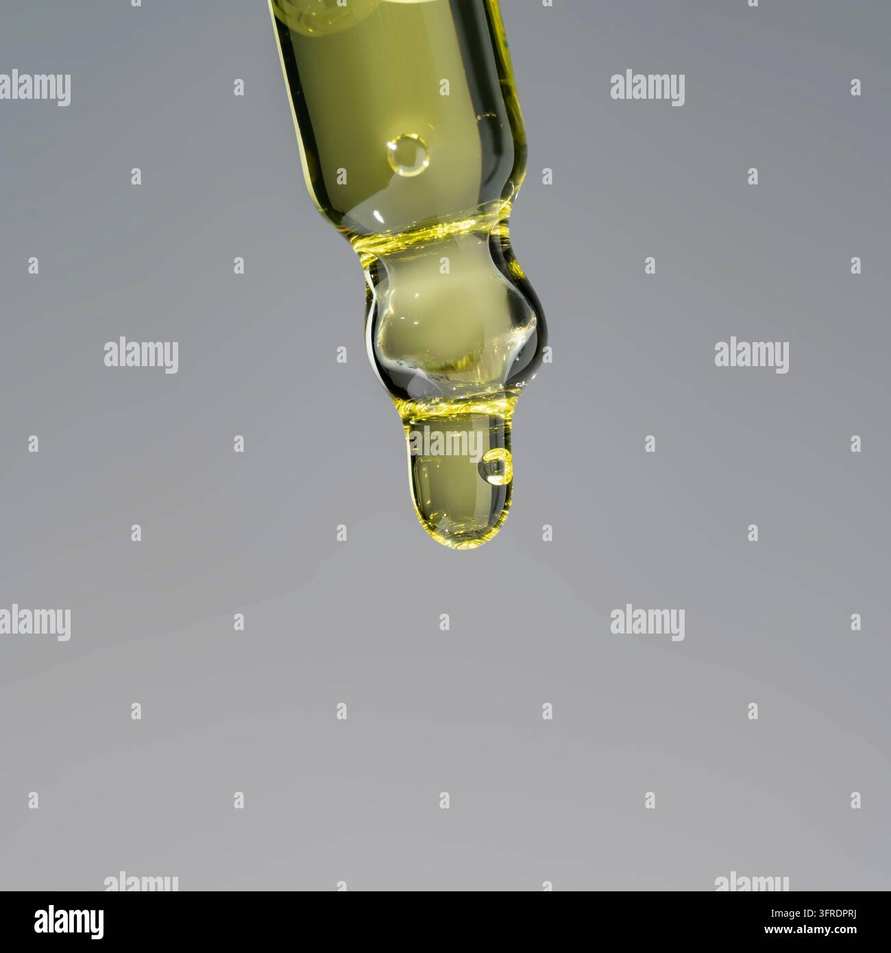 Öltropfen, der aus einer Pipette in eine Kosmetikflasche tropft, Nahaufnahme, isoliert auf grauem Hintergrund. Hautpflegeproduktpräsentation Stockfoto
