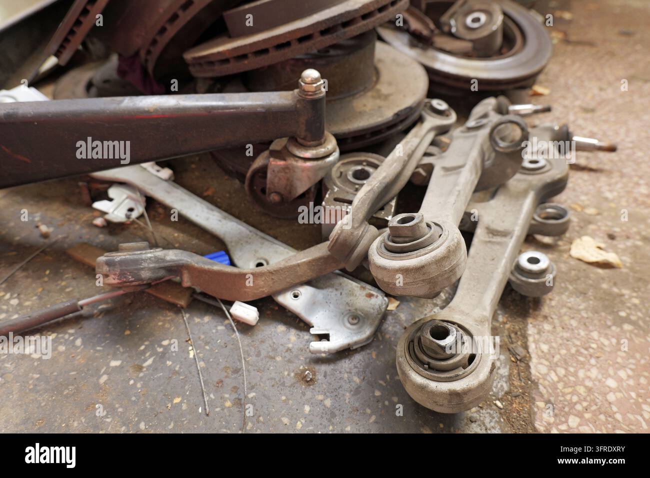 Gebrauchte und rostige Autoaufhängungslenker, Kugelgelenke und Bremsscheiben, die auf einem Betonboden in der Garage liegen, repräsentieren Autoreparatur und Wartung Stockfoto