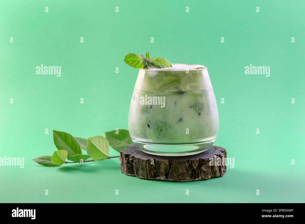 Eisgekühlter grüner Matcha-Tee gemischt mit Eiswürfeln und Milch in einem Latte-Glas auf grünem Hintergrund. Konzept eines eisigen Sommergetränks Stockfoto
