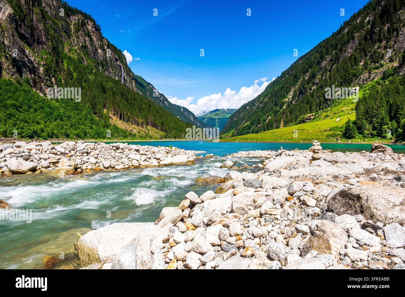 Türkisches Wasser des Stausees Stillup in der Nähe von Mayrhofen in den Zillertaler Alpen, Tirol, Österreich. Felsiger Fluss im Vordergrund mit Geröll und schneller Strömung Stockfoto