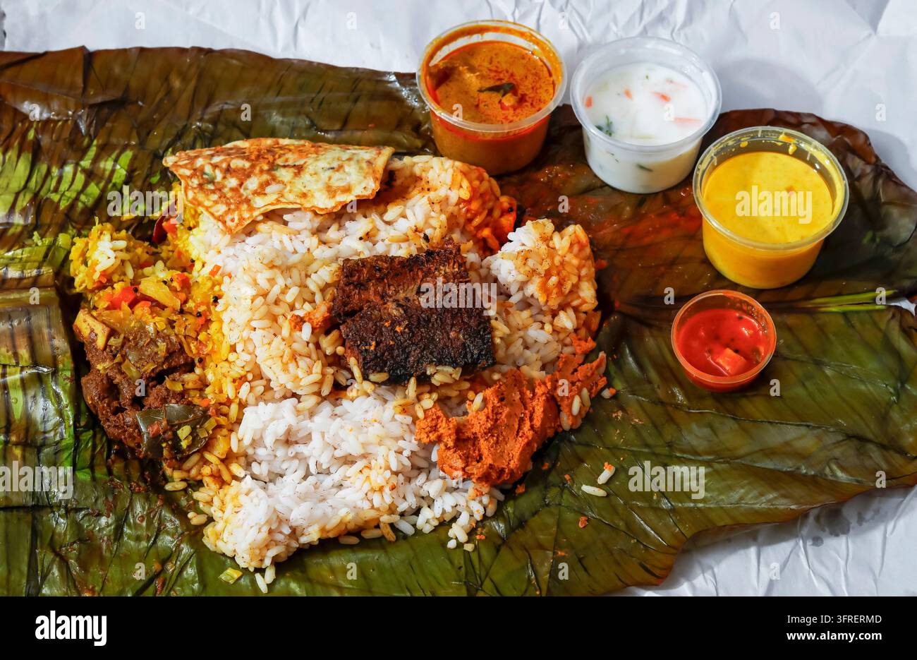 Traditionelles südindisches Pothi-Choru-Reisparcel, geöffnet auf Bananenblatt mit gebratenem Fisch, Omelett, Currys und Pickle Stockfoto