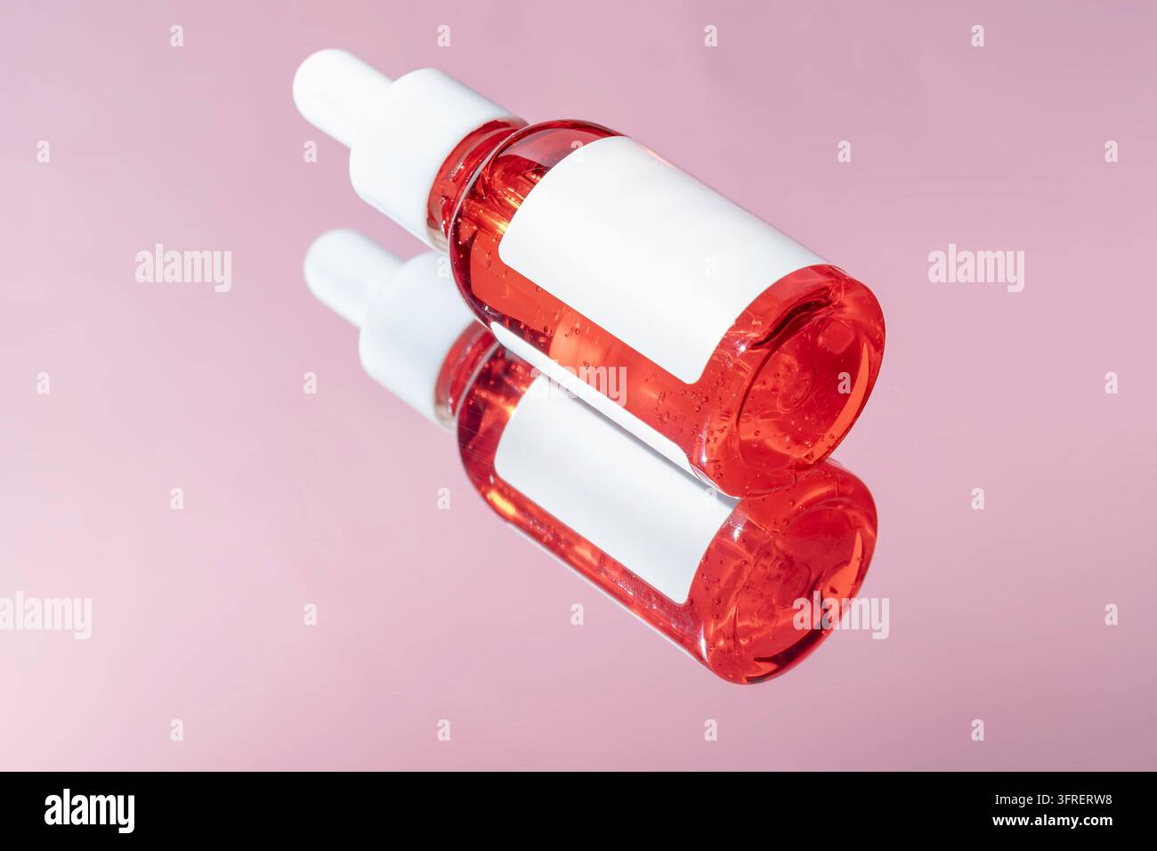 Dropper-Glas-Flaschen-Mock-Up. Dropper-Pipette mit Serum oder ätherischem Öl auf rosa Hintergrund mit Reflexion für die Produktpräsentation. Hautpflegekosmetik Stockfoto