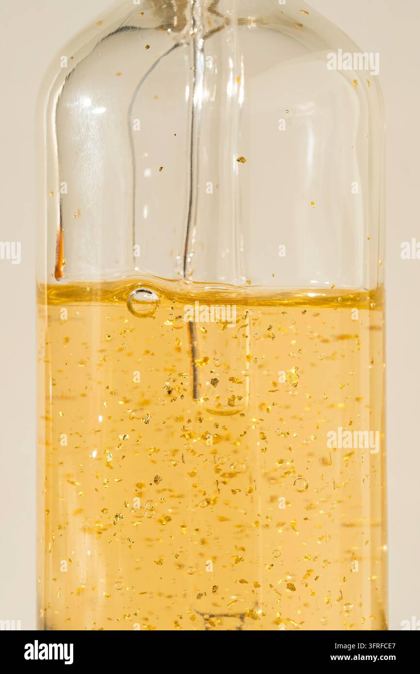 Serumpipette mit 24K-Goldpartikeln, die auf die Flasche tropfen, auf beigem Hintergrund. Kosmetikprodukt Stockfoto