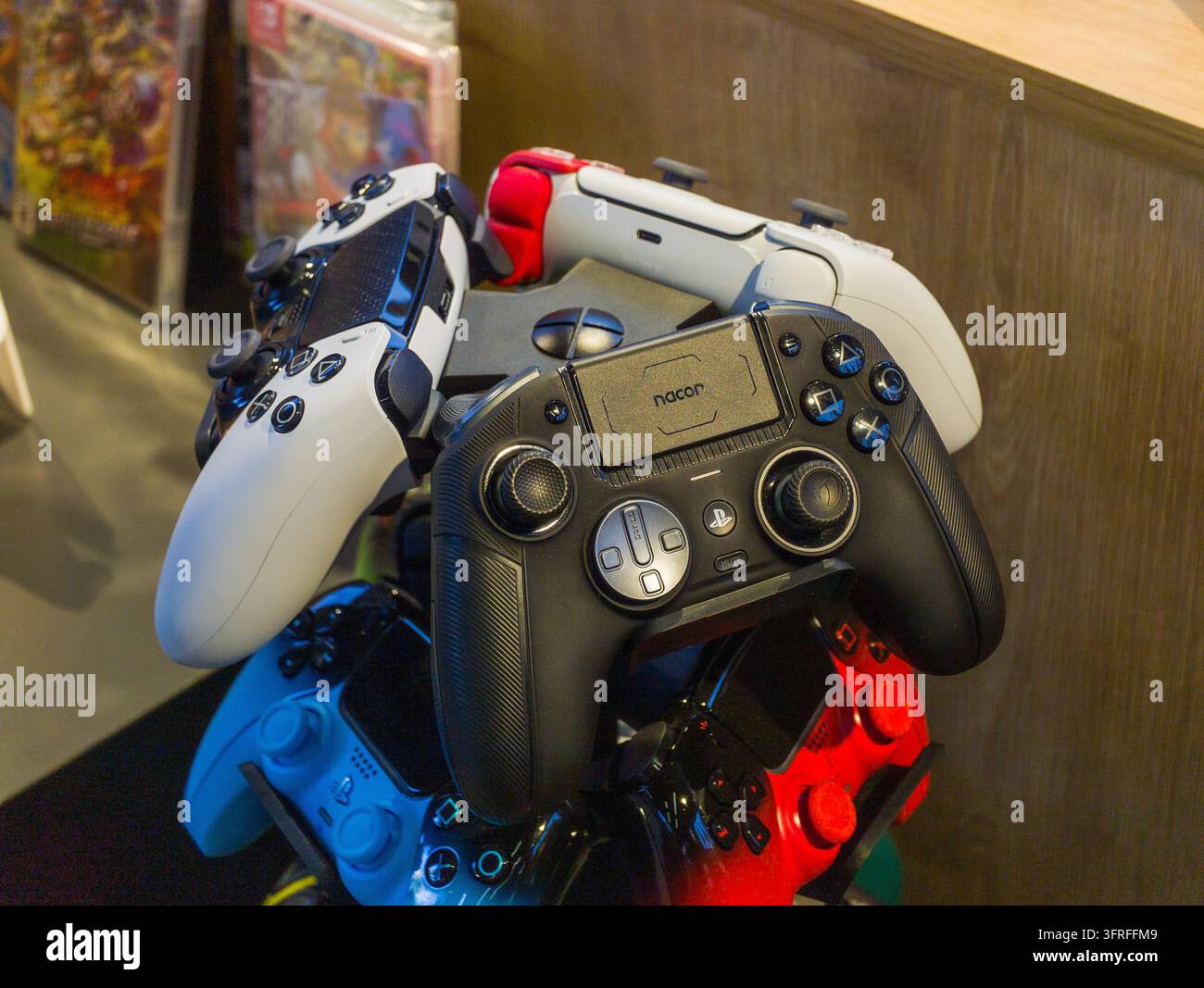 Gestapelte Videospiel-Controller in verschiedenen Farben. Schwarze, weiße, blaue und rote Controller. Controller liegen auf einer Holzoberfläche. Hintergrund zeigt Unschärfe Stockfoto