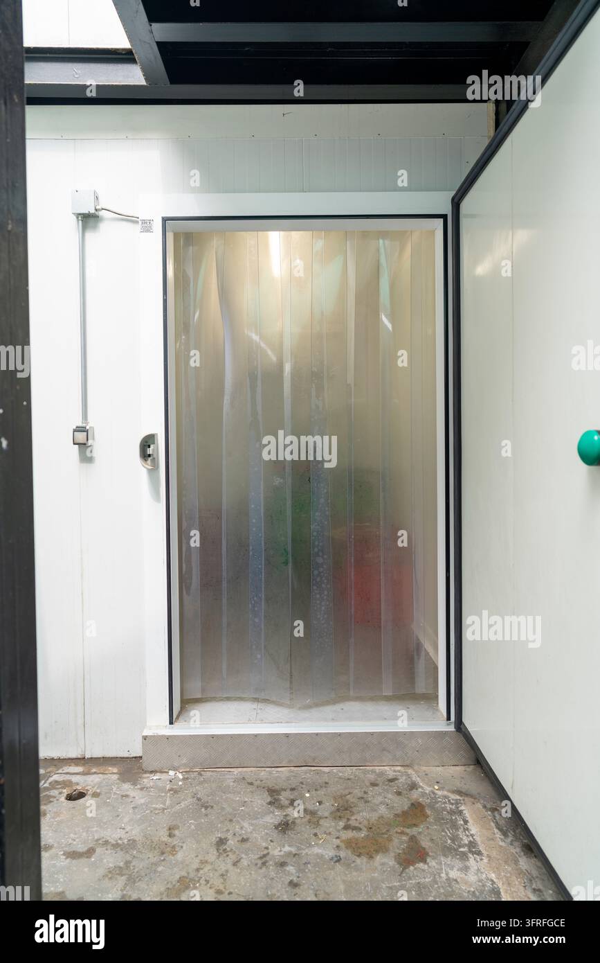 Transparenter PVC-Lamellenvorhang an einer isolierten Industrietür für Kältelagerung, Lebensmittelverarbeitung und Temperaturkontrolle. Stockfoto