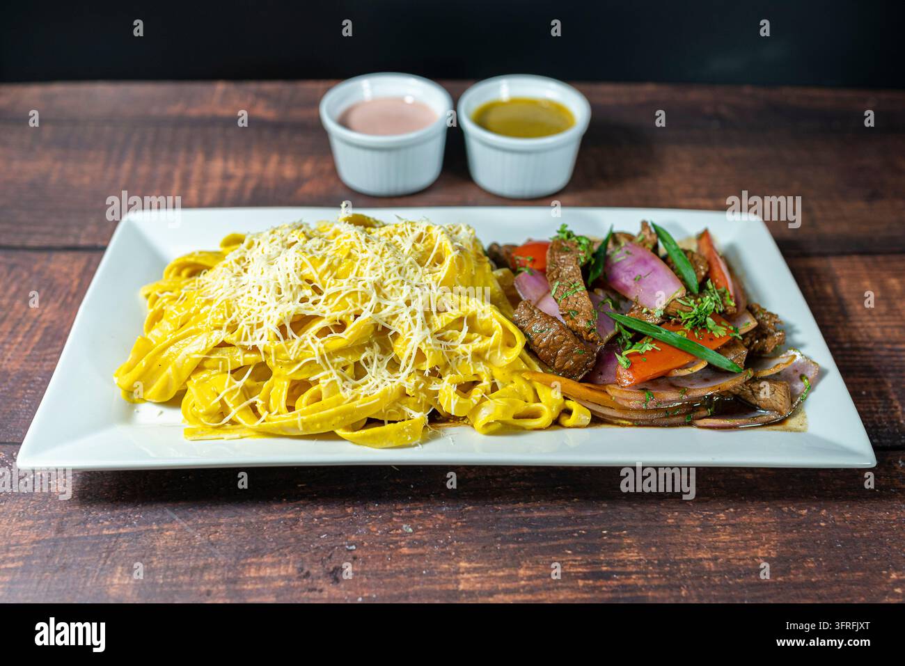 Peruanisches Lomo Saltado serviert mit cremiger Huancaina-Pasta, ein Fusion-Gericht, das klassische Aromen und Traditionen kombiniert. Stockfoto