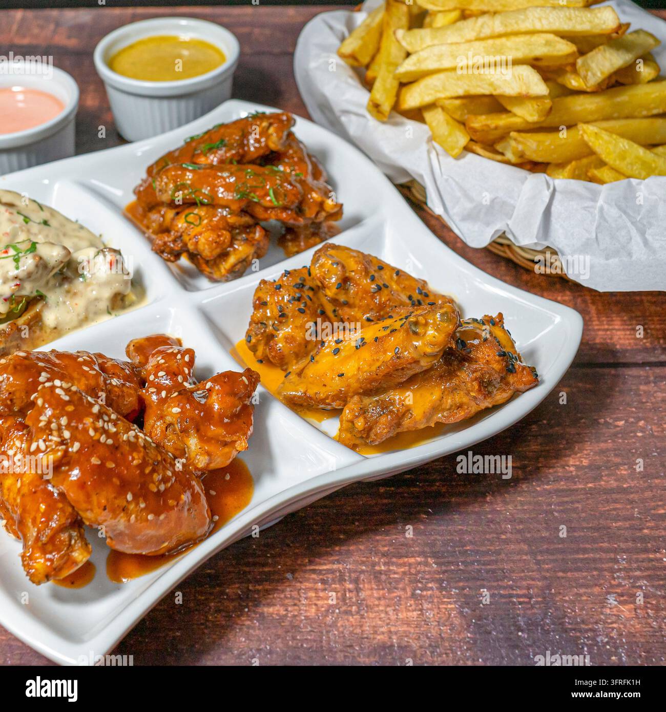 Verschiedene Hühnerflügel mit verschiedenen Saucen und Pommes frites, geschmackvolles Vorspeisenplatte perfekt zum Teilen von Mahlzeiten. Stockfoto