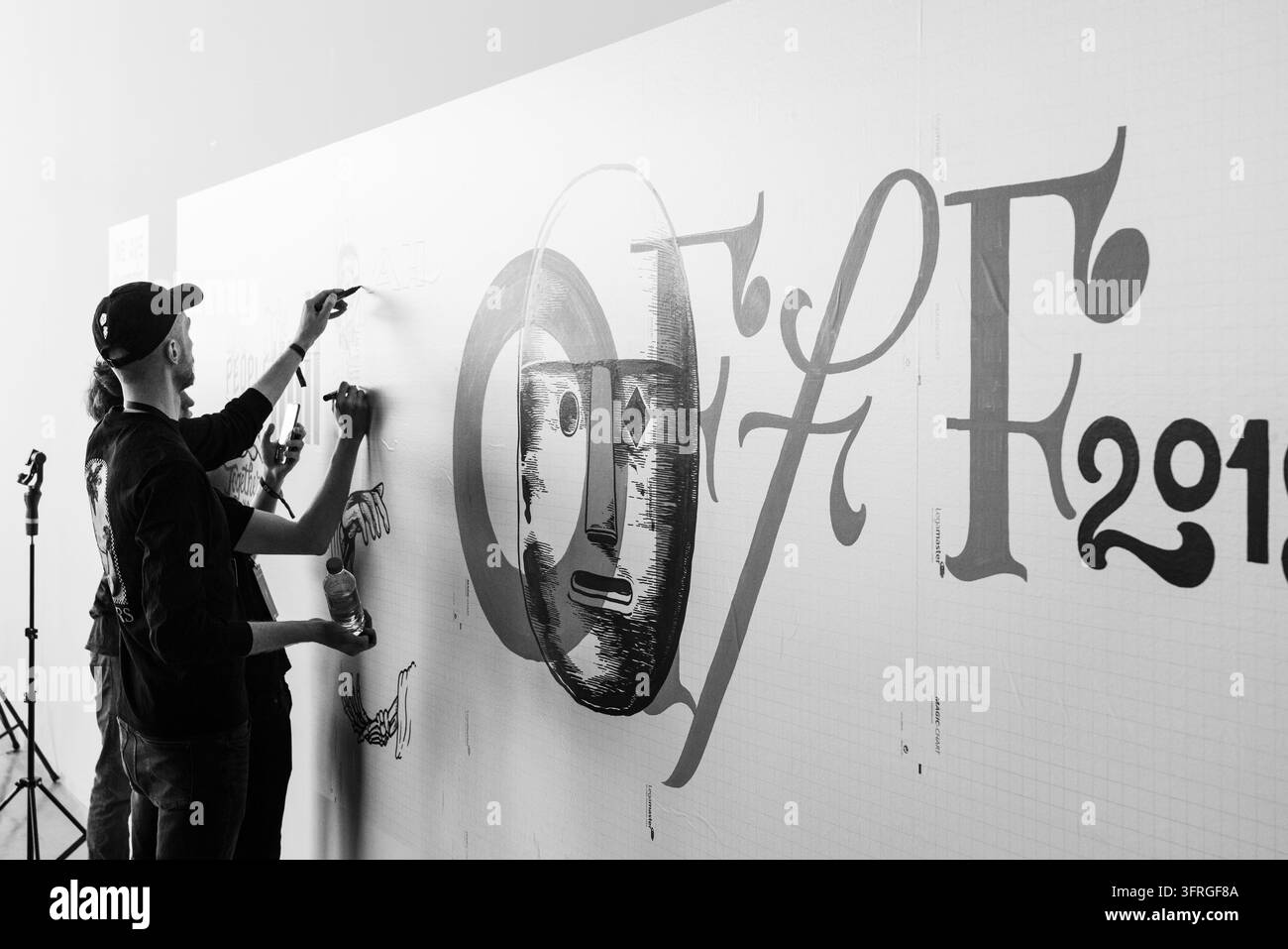KÜNSTLER KOOPERIEREN BEI LEBENSDRAWING IN SCHWARZ WEIß, OFFF FESTIVAL 2019 REPORTAGE, BARCELONA, SPANIEN: In einer Schwarz-Weiß-Fotografie stehen drei männliche Künstler und zeichnen an einer großen Wand mit Typografie und einem grafischen Gesicht. INFO: Die OFFF-Konferenz wurde 2001 ins Leben gerufen und ist die weltweit größte Bühne für zeitgenössische visuelle Kreativität und Design. Sie zieht die besten Designer, Künstler, Filmemacher und Fotografen der Welt an. Sie dient als globale Plattform für kreativen Austausch und Zusammenarbeit. Stockfoto