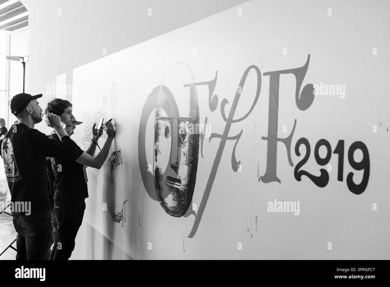 TEAM VON KÜNSTLERN BEI DER ARBEIT IN SCHWARZ-WEISS, BARCELONA OFFF FESTIVAL 2019 REPORTAGE, BARCELONA, SPANIEN: In Schwarz-Weiß aufgenommen, zeichnen zwei Männer eine große Wandgrafik, während ein anderer sie mit einem Telefon filmt oder fotografiert. INFO: Die OFFF-Konferenz wurde 2001 ins Leben gerufen und ist die weltweit größte Plattform für zeitgenössische visuelle Kreativität und Design. Sie zieht die besten Designer, Künstler, Filmemacher und Fotografen der Welt an. Sie dient als globale Plattform für kreativen Austausch und Zusammenarbeit. Stockfoto