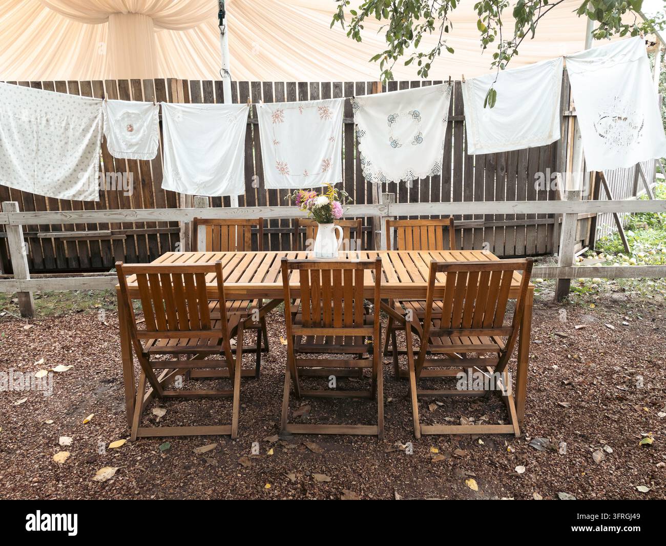 Rustikales Outdoor-Essensarrangement mit Holztisch und hängenden bestickten Leinen - Smartphone-aufgenommenes Stockfoto