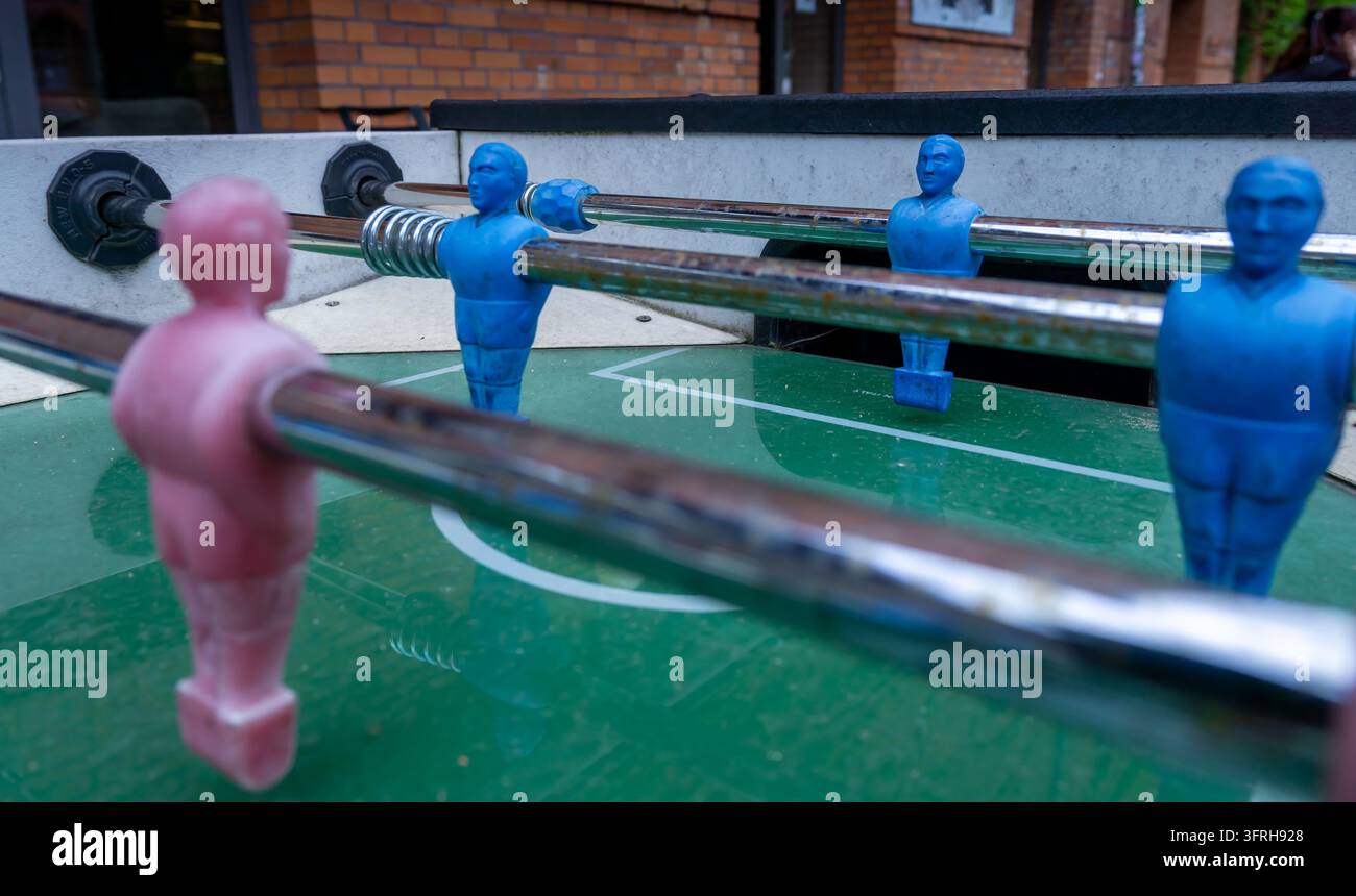 Eine Nahaufnahme zeigt ein Tischfußballspiel, bei dem blaue und rosa Spielerfiguren auf Metallstangen angeordnet sind. Stockfoto