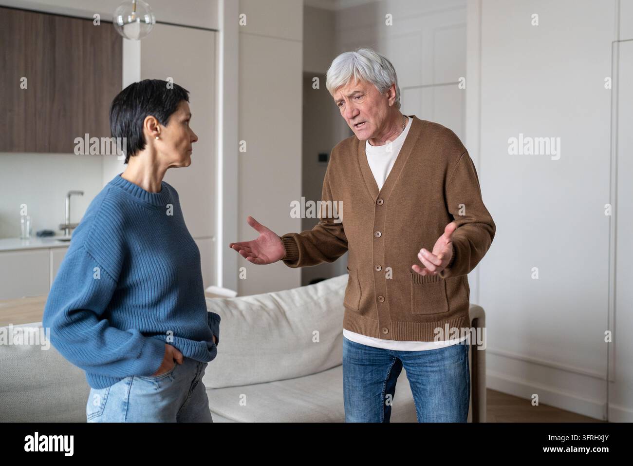 Gestresster besorgter älterer Ehemann streitet mit unbeeindruckter enttäuschter Ehefrau im Wohnzimmer. Stockfoto