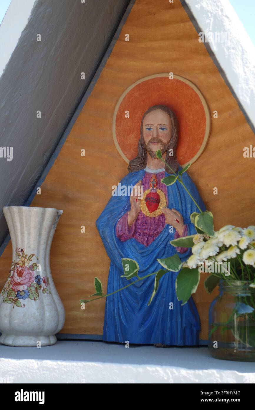 Kleiner Straßenaltar mit einem Relief des Heiligsten Herzens Jesu und frischen Blumen in einer Vase im Vipava-Tal, Slowenien. Stockfoto