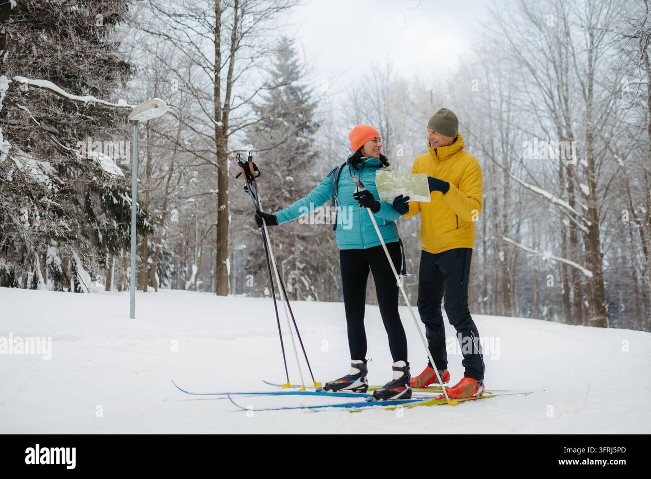 Seniorenpaar auf Langlaufski steht in einem verschneiten Wald und liest gemeinsam eine Karte. Stockfoto