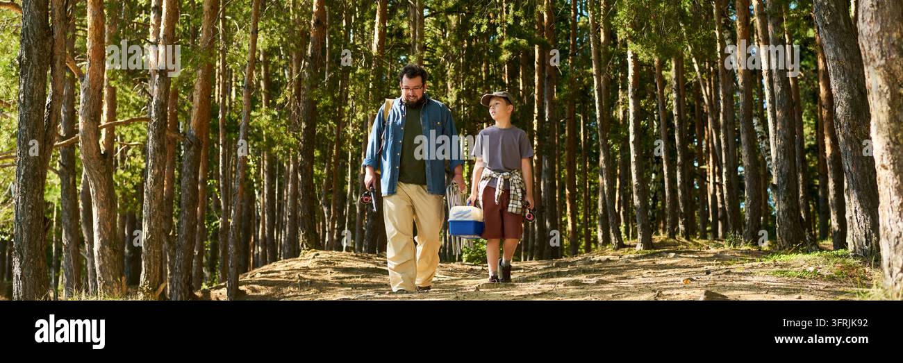 Vater und Junge gehen durch Kiefernwald zum Angeln Stockfoto