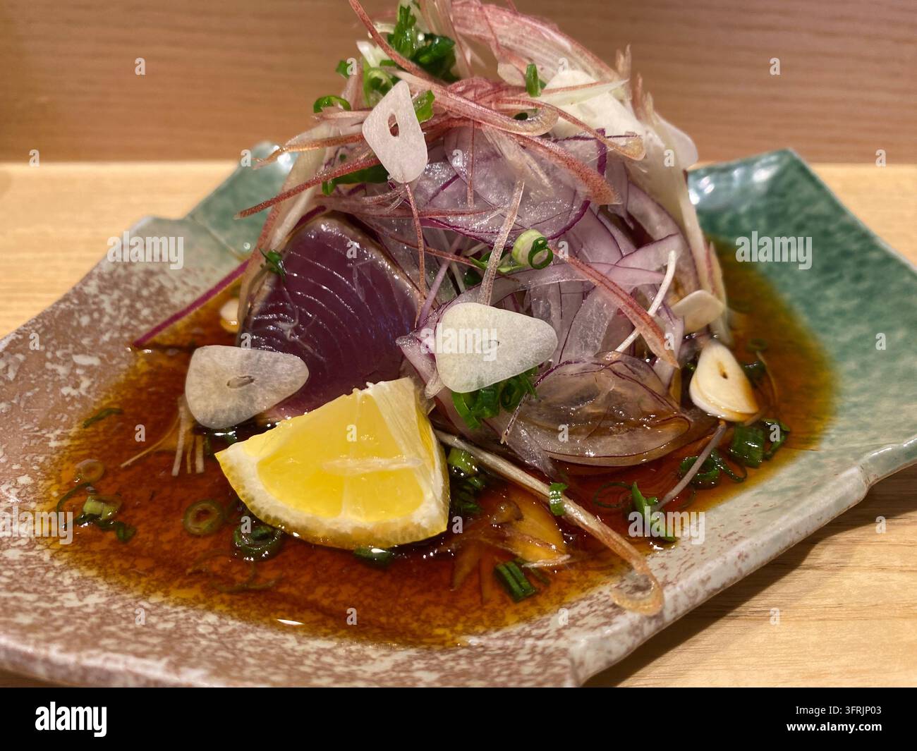 Nahaufnahme von frisch gebratenem Bonito-Sashimi (Katsuo no Tataki) mit Garnierungen, serviert in einem japanischen Restaurant in Fukuoka, Japan. - Smartphone-aufgenommenes Stockfoto