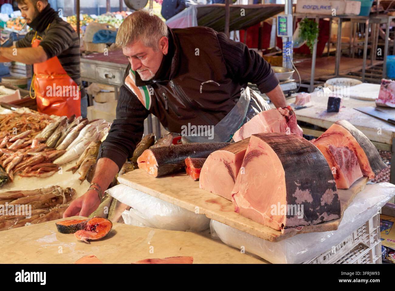 Ein Händler arrangiert Schwertfisch- und Lachsstücke auf einer Marmorplatte auf dem Pescheria-Freiluft-Fischmarkt in Italien an einem Dezembermorgen. Stockfoto