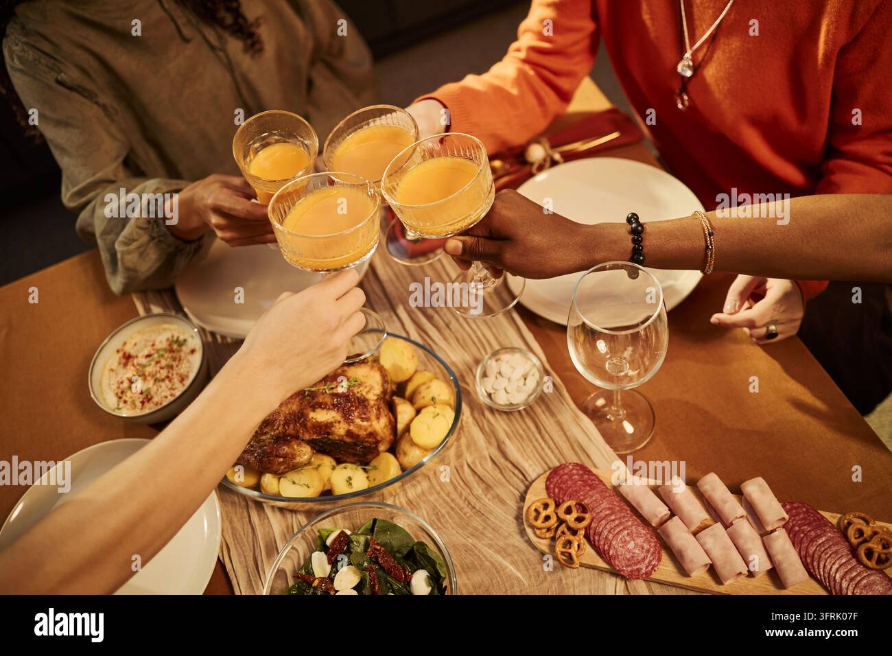 Multikulturelle Freunde stoßen mit Getränken bei einem festlichen Abendessen an Stockfoto
