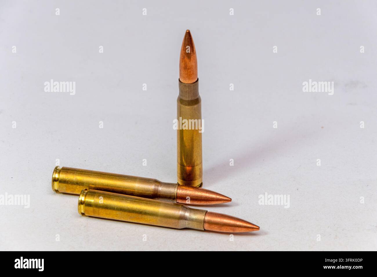Drei Gewehrpatronen sind auf einem weißen Hintergrund angeordnet, wobei eine aufrecht steht. Stockfoto